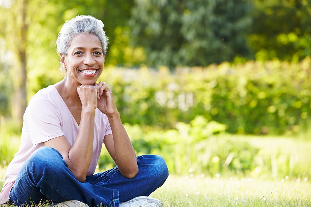 A woman sitting outdoors in a park on a summer day, smiling
